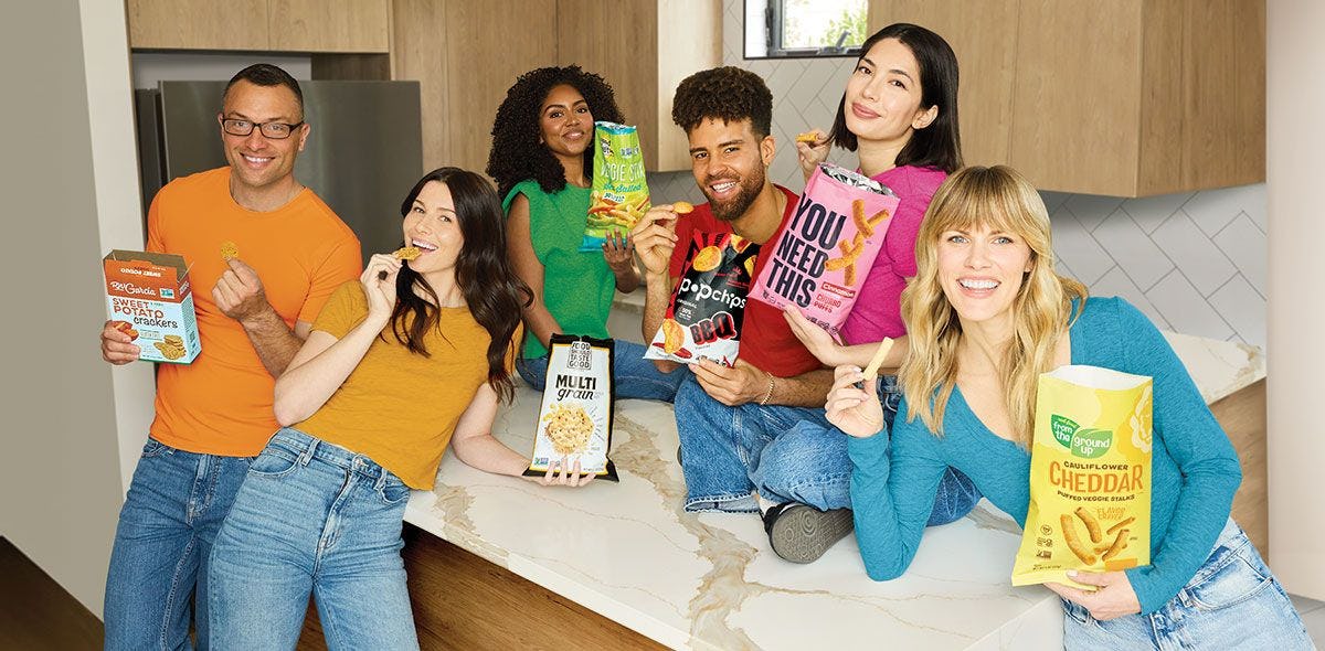 Six people holding various bags of snacks and smiling at the camera.